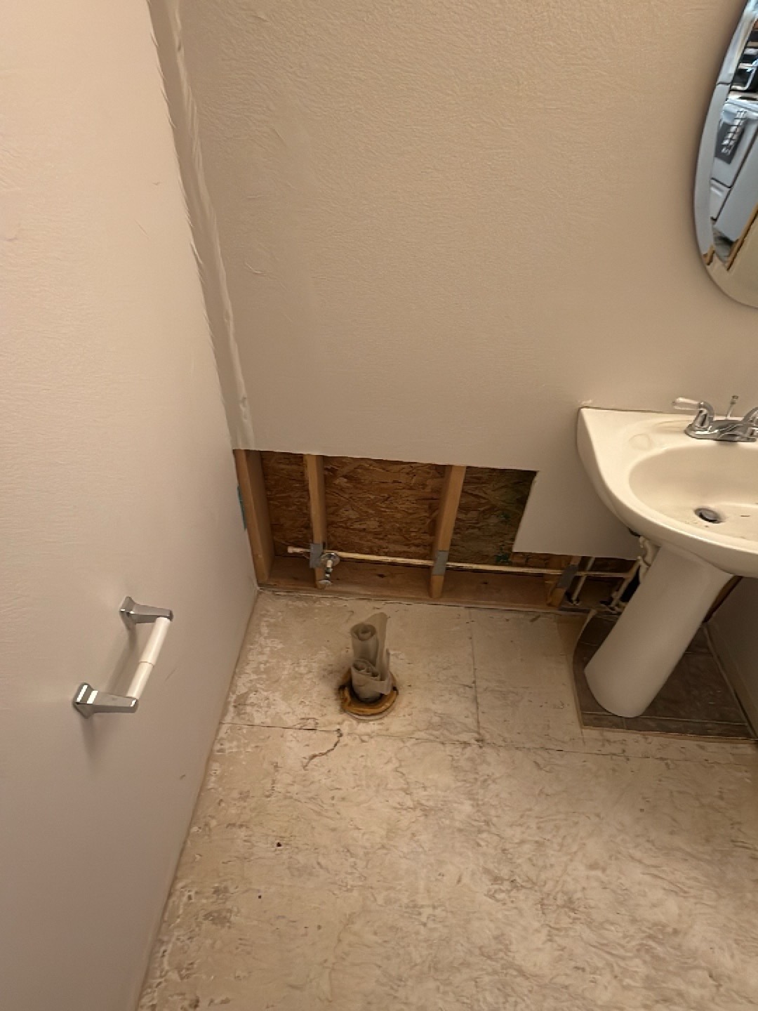 Bathroom after mitigation with toilet removed, lower drywall cut away exposing wall cavity, studs, and subfloor