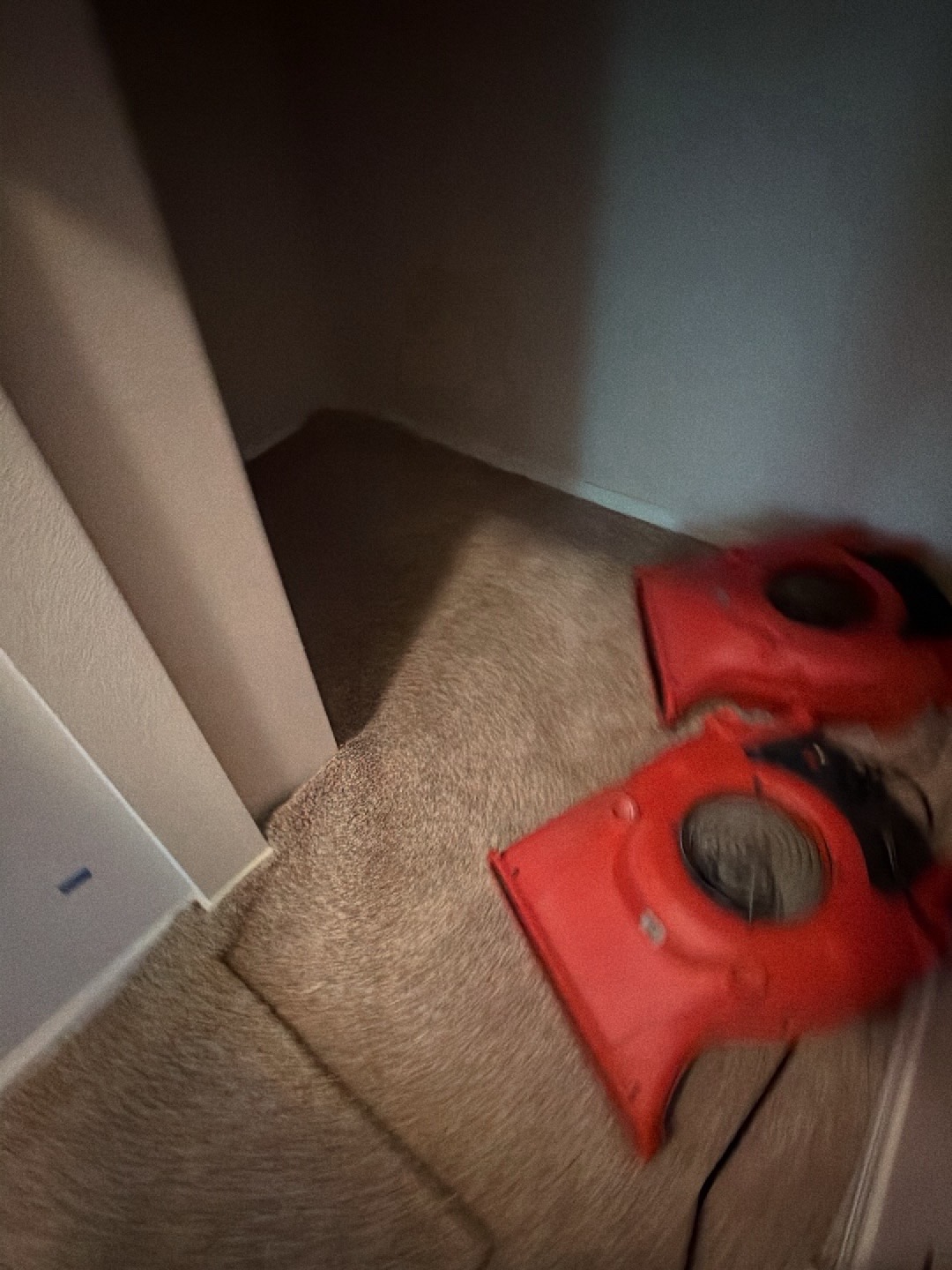 Under-stairs closet with two red air movers placed on tan carpet to dry the confined space and baseboards