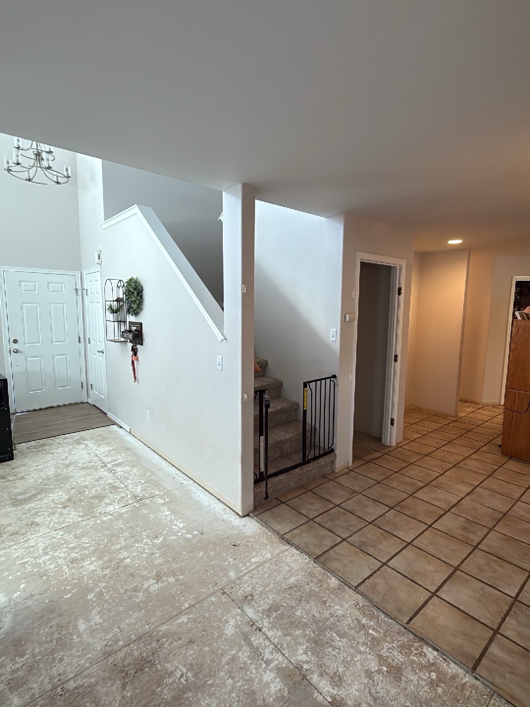 Hallway floor transition after mitigation, subfloor exposed next to intact tile, safety gate at stairs