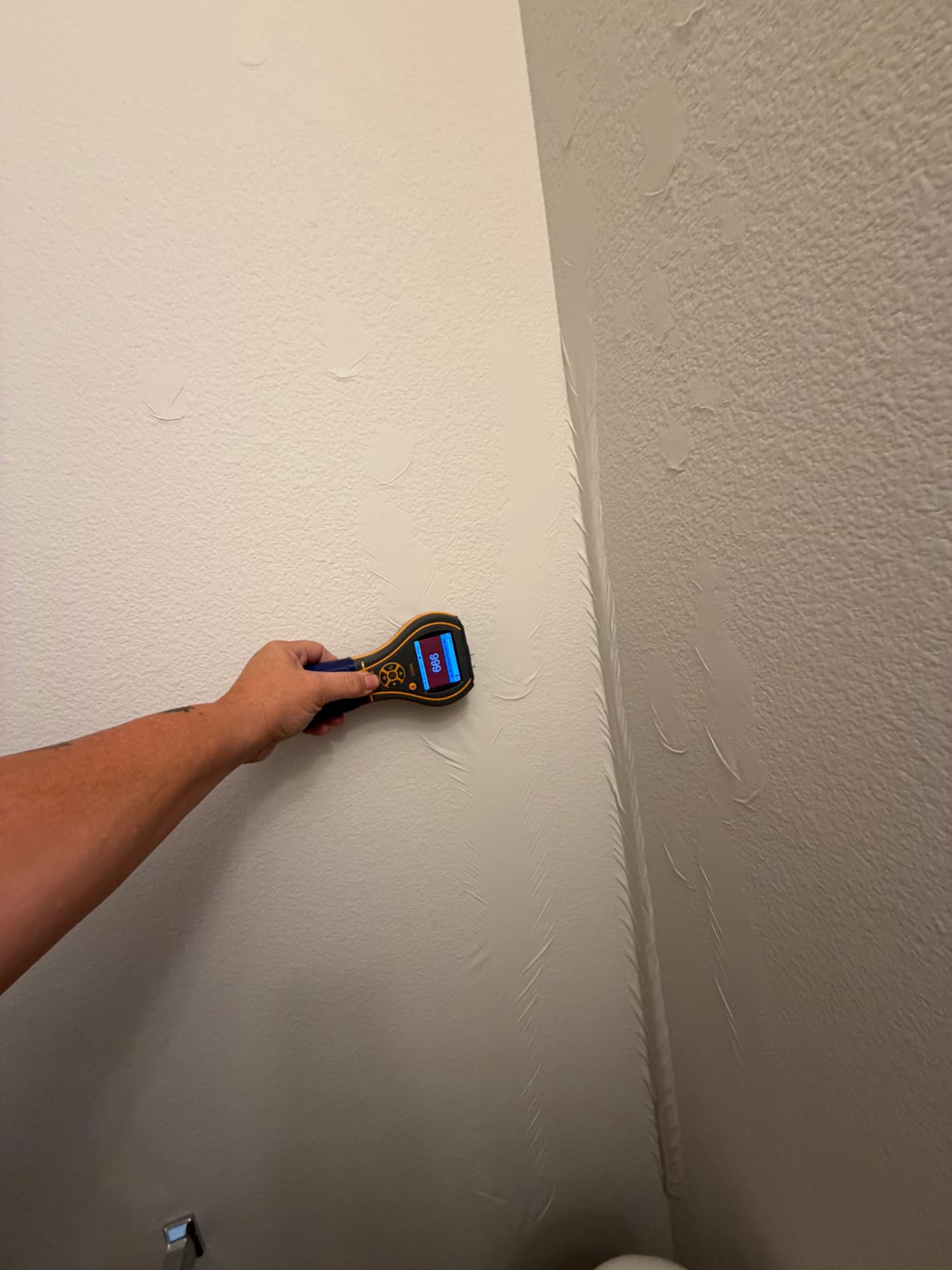 Protimeter MMS3 moisture meter reading 999 on bathroom drywall with visible bubbling tape behind the toilet