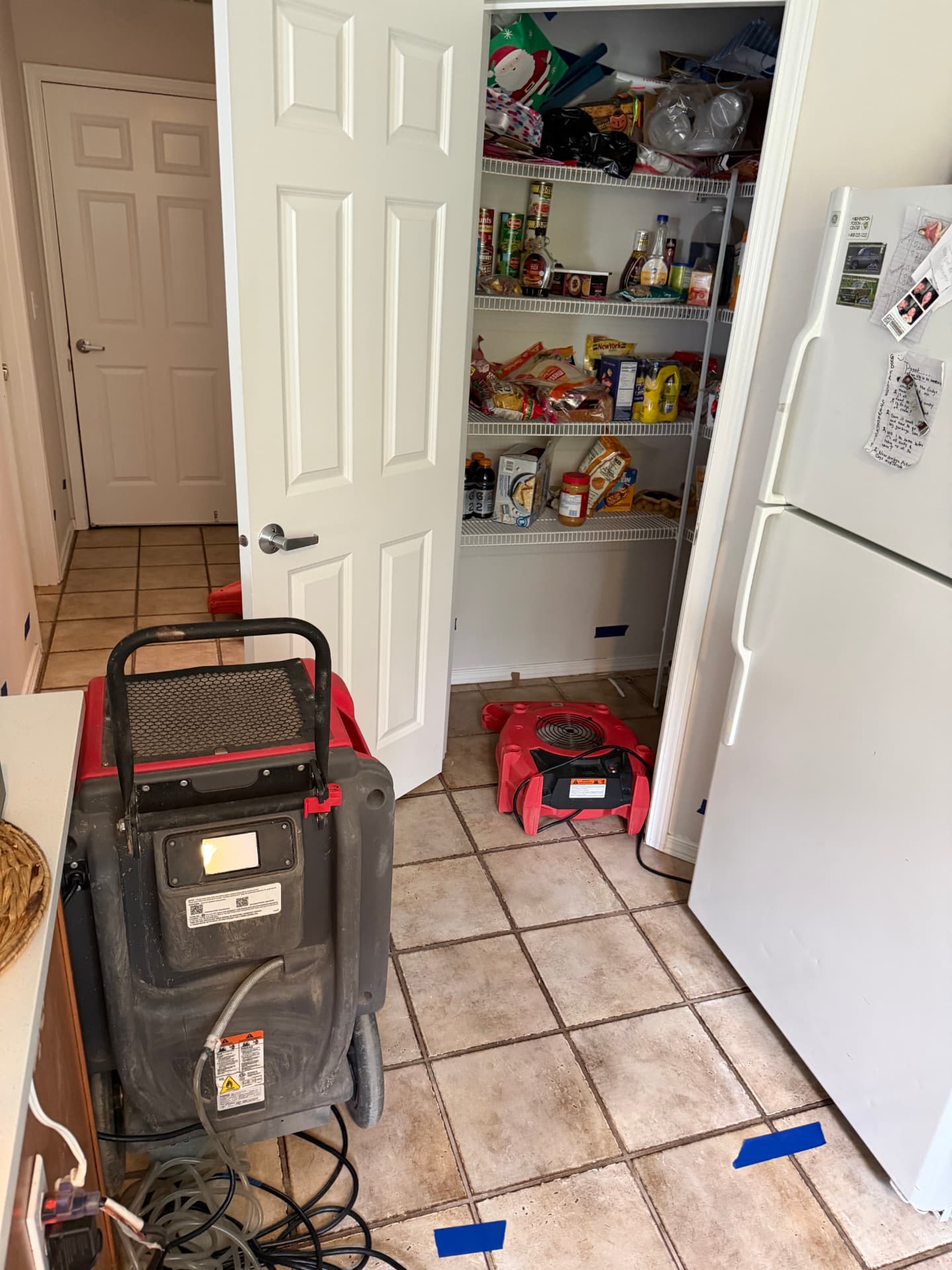 Kitchen with an LGR dehumidifier running and a red air mover placed inside the open pantry, blue tape marks on the tile floor