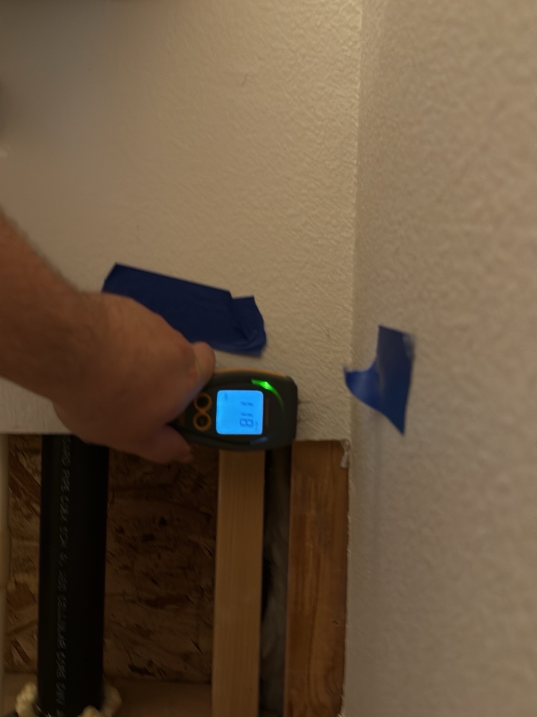 Moisture meter reading 11.8 with green status light on drywall after mitigation, confirming the wall is dry