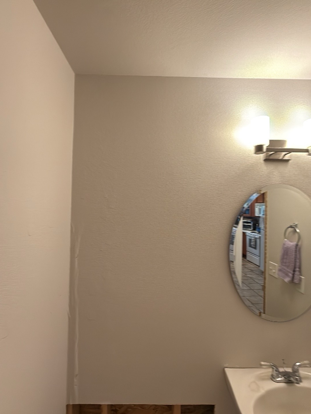 Bathroom wall detail after mitigation, upper wall intact above the cut line, mirror reflecting kitchen